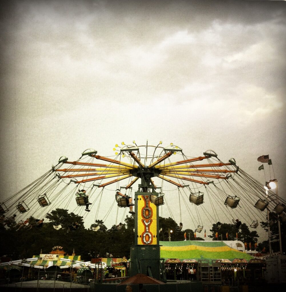 A tall swing ride spinning above the fairground tents at dusk at the Barnstable County Fair