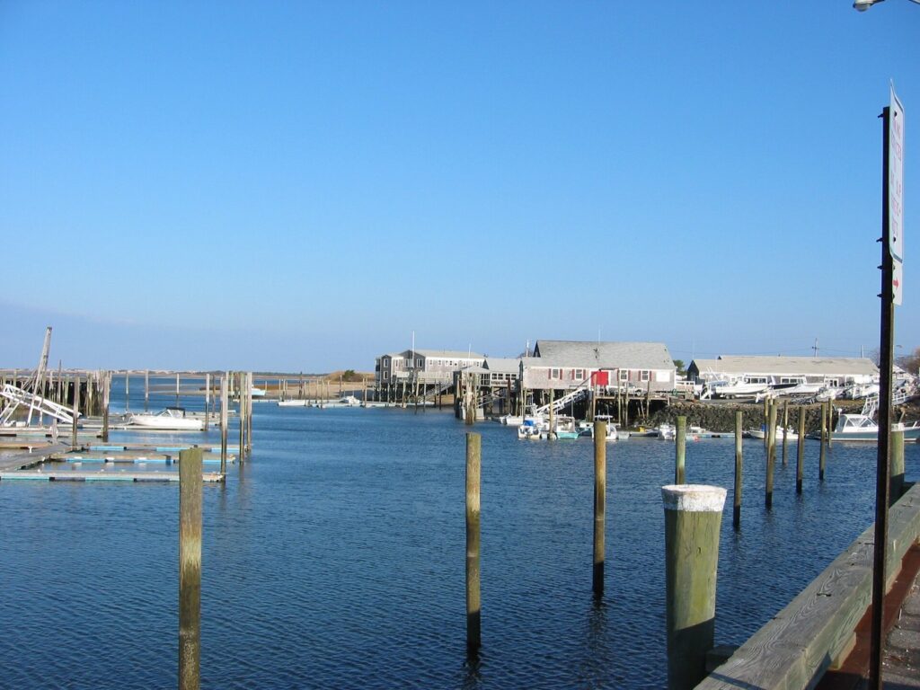 Wooden pilings, floats and waterfront buildings at Barnstable Harbor under a clear blue sky