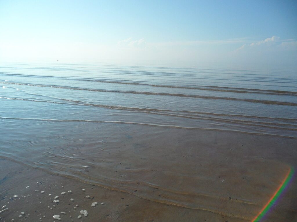 Calm shallow water and wet sand stretching to the horizon on the tidal flats of Cape Cod Bay at East Brewster