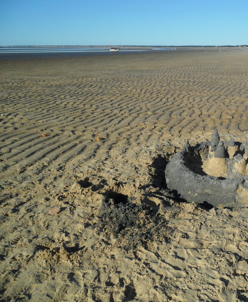 A sandcastle and rippled sand on the Brewster tidal flats at low tide, with the distant water under a blue sky