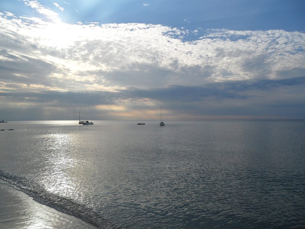 Evening light breaking through clouds over calm Cape Cod Bay, with a few boats at anchor