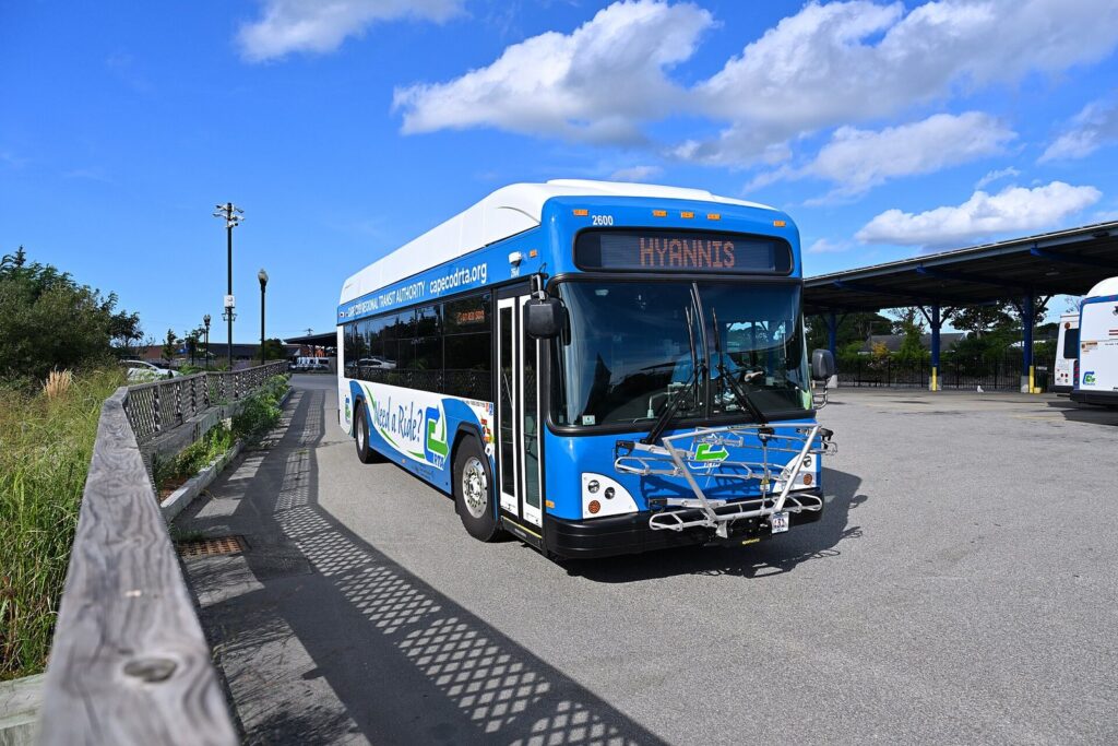 A blue and white CCRTA battery-electric bus signed for Hyannis pulling into the bus depot on a sunny day