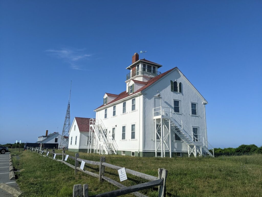 The white former Coast Guard station with a red roof and lookout tower above the parking area at Coast Guard Beach in Eastham
