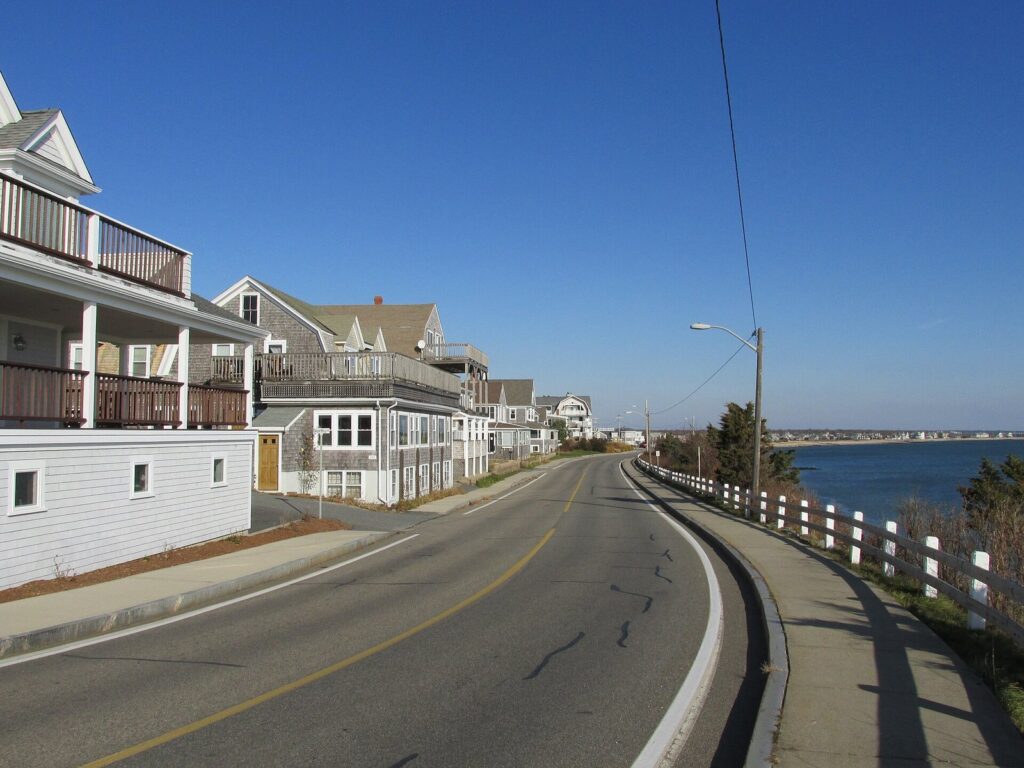 Houses and inns along Grand Avenue in Falmouth Heights, with a white rail and Nantucket Sound to the right