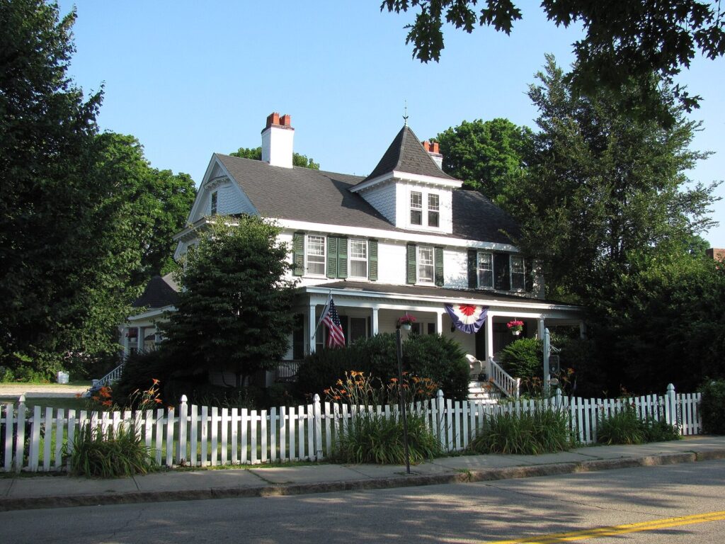 A white house with a picket fence, an American flag and red, white and blue bunting near the Village Green in Falmouth