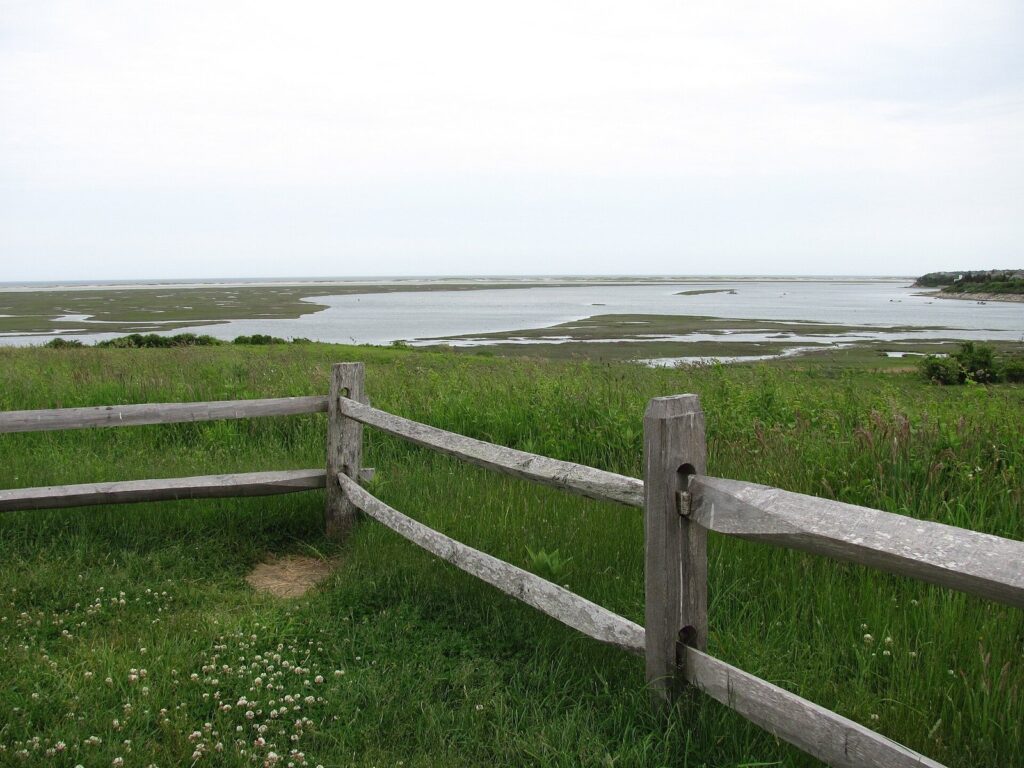 A split-rail fence and green meadow at Fort Hill in Eastham, overlooking the channels of Nauset Marsh