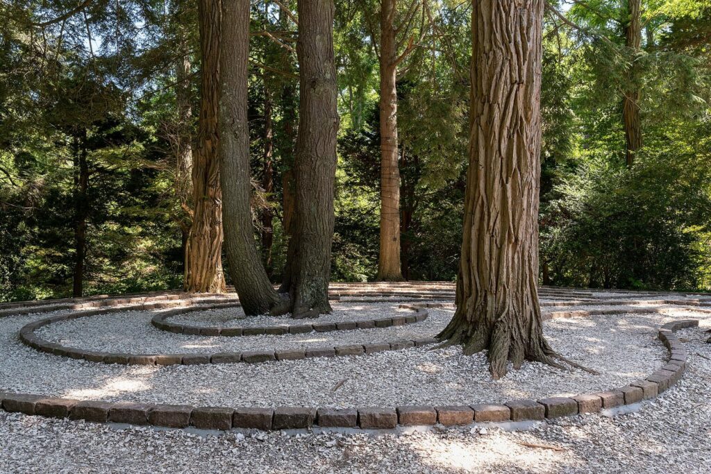 A circular stone-edged labyrinth path on gravel among tall trees in the gardens at Heritage Museums and Gardens in Sandwich