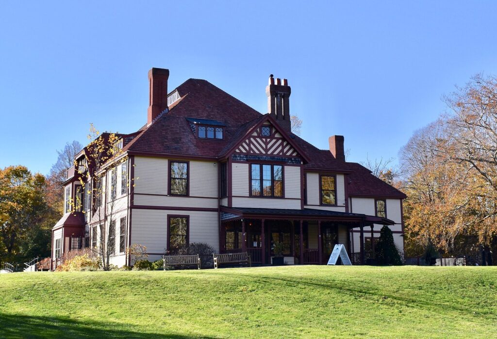 Highfield Hall, a large Victorian house with red trim and tall chimneys, on a green lawn in Falmouth under a blue sky