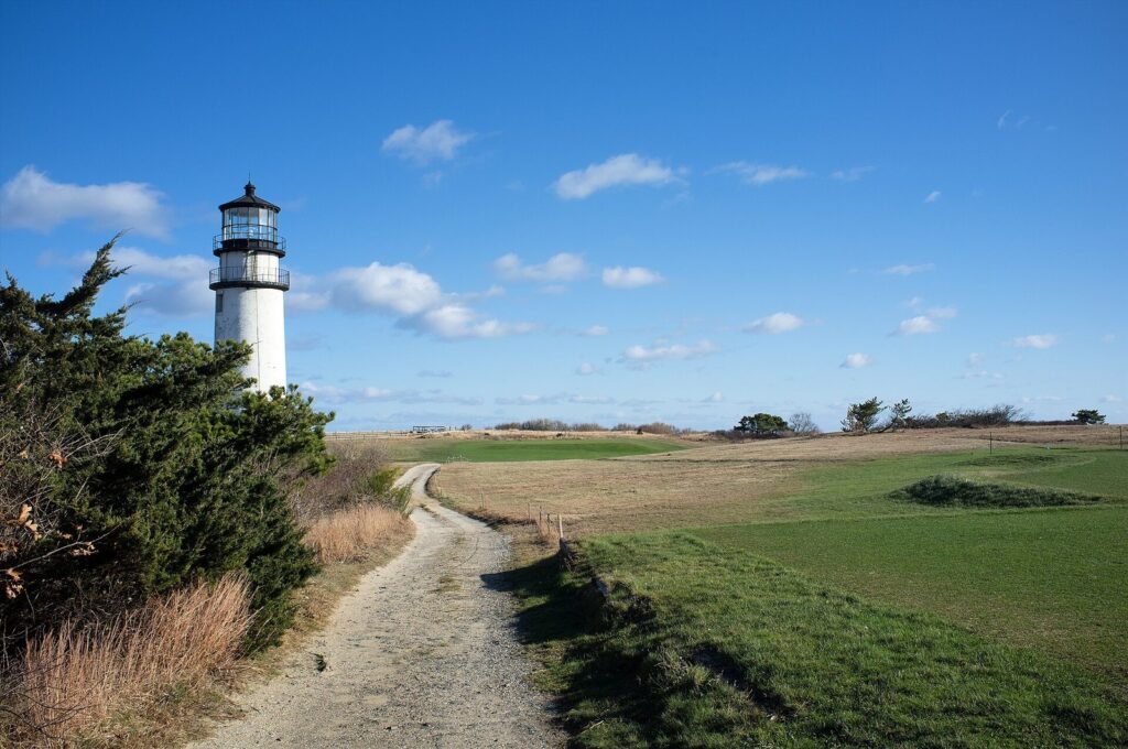 Highland Light's white tower at the end of a gravel path through open grassland in Truro