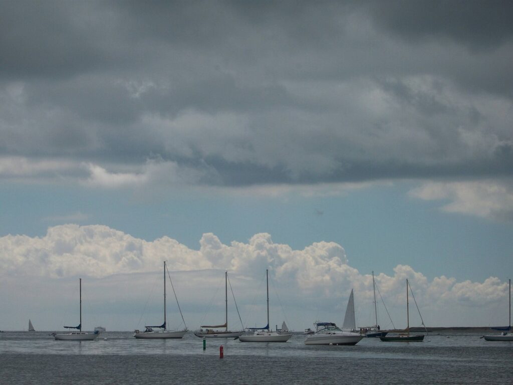 Sailboats and a motorboat on moorings in Lewis Bay under a dark band of storm clouds