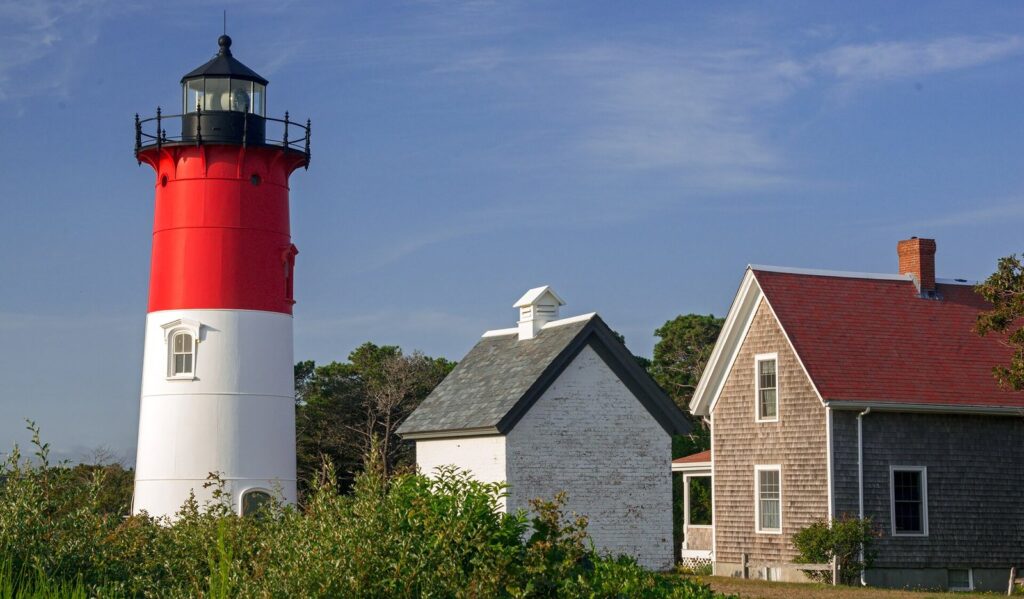 Nauset Light's red and white tower beside a small white brick oil house and a shingled keeper's house with a red roof in Eastham
