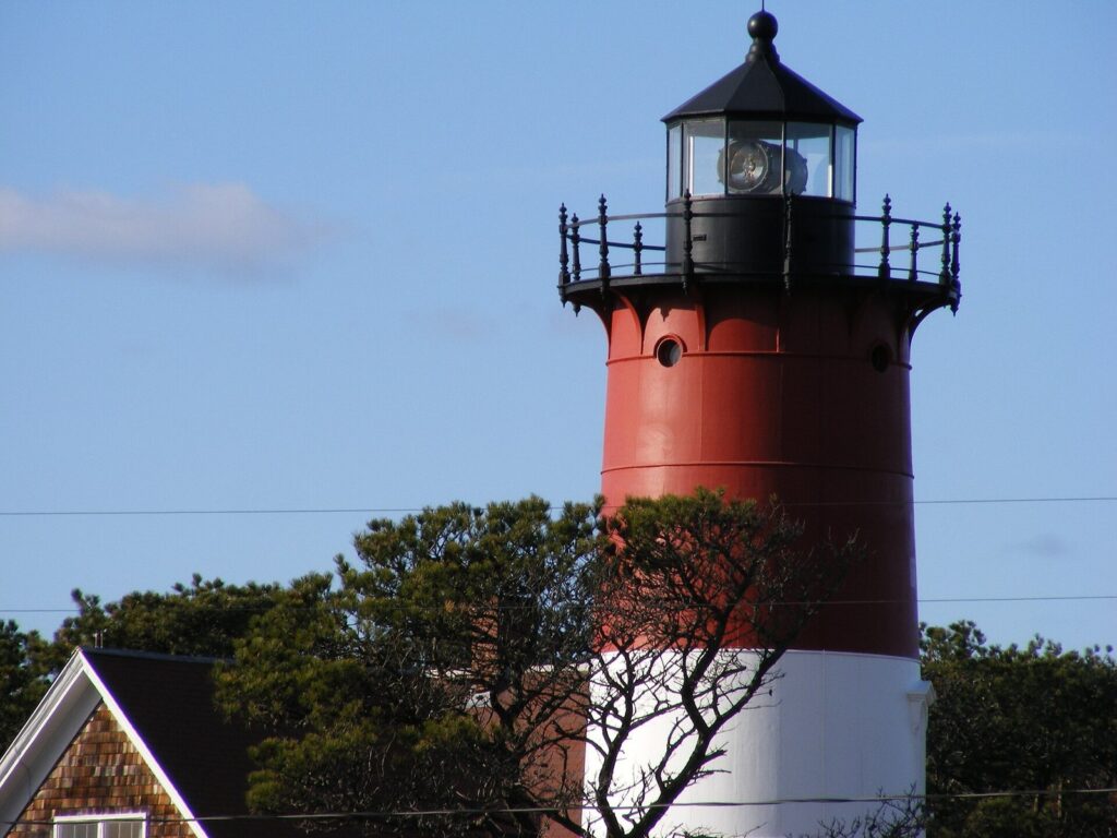 The red and white tower of Nauset Light against a blue sky, with pitch pines around its base