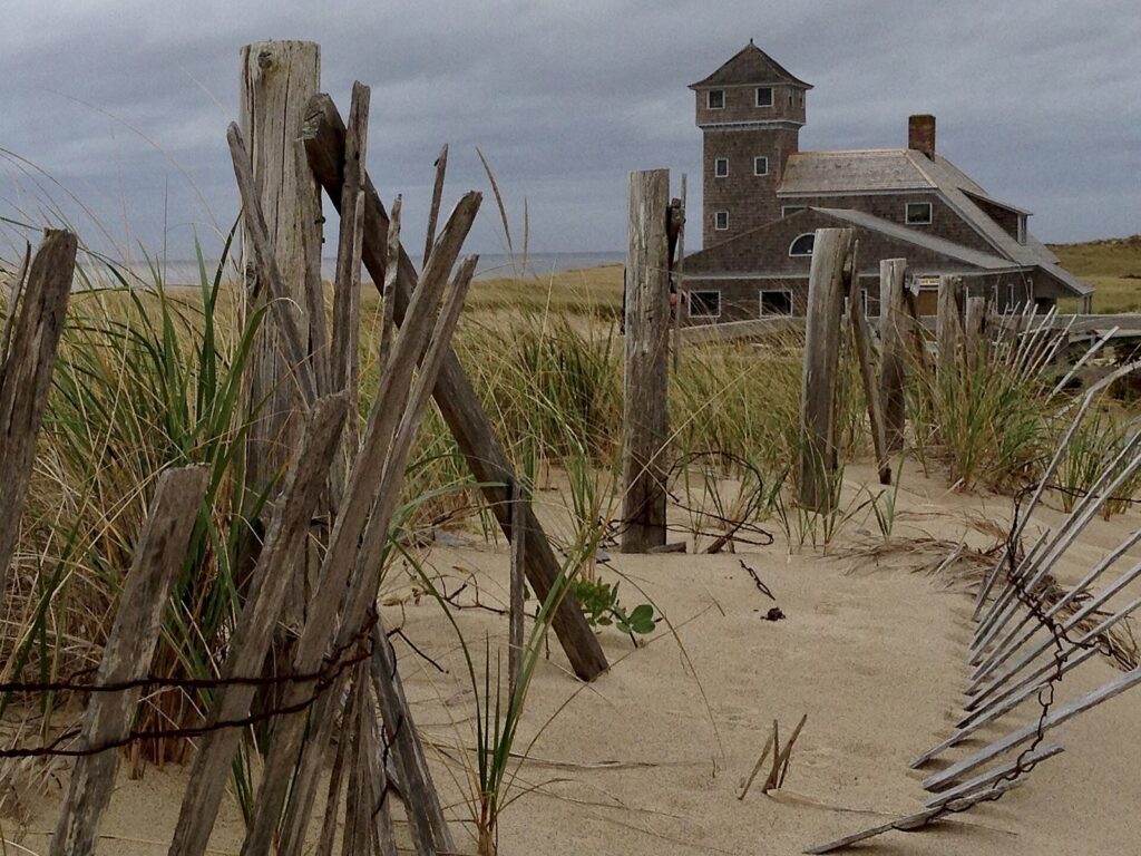 The shingled Old Harbor Life-Saving Station with its lookout tower, seen through weathered dune fencing at Race Point