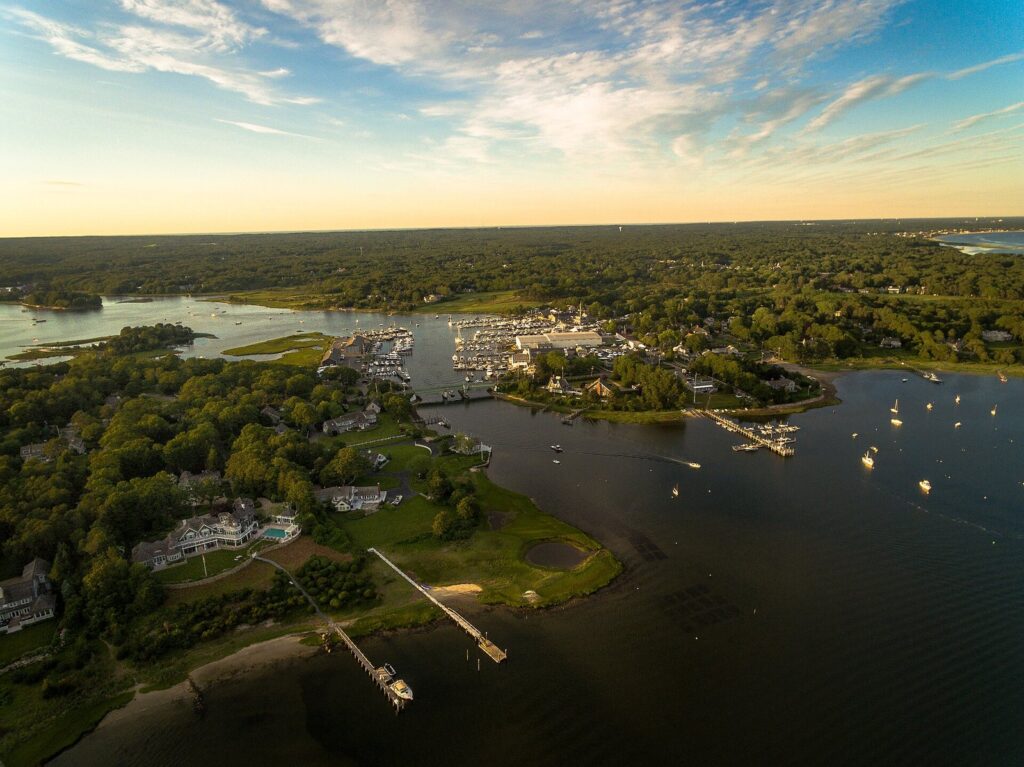 Aerial view of Osterville's West Bay with moored boats, docks and wooded shoreline in low evening light