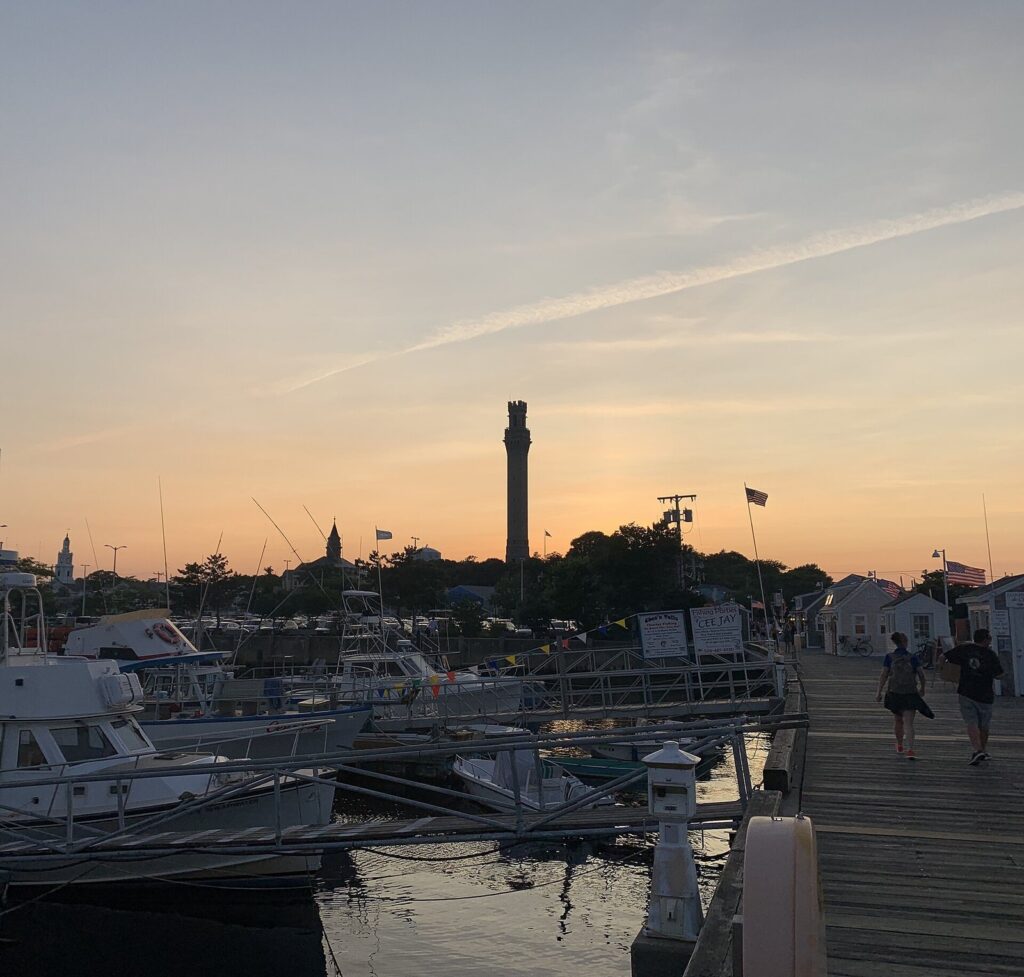 Pilgrim Monument silhouetted above Provincetown's harbor docks after sunset
