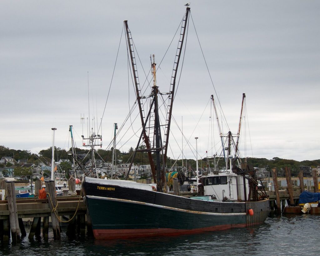 A green-hulled fishing dragger with tall outriggers tied up at a pier in Provincetown