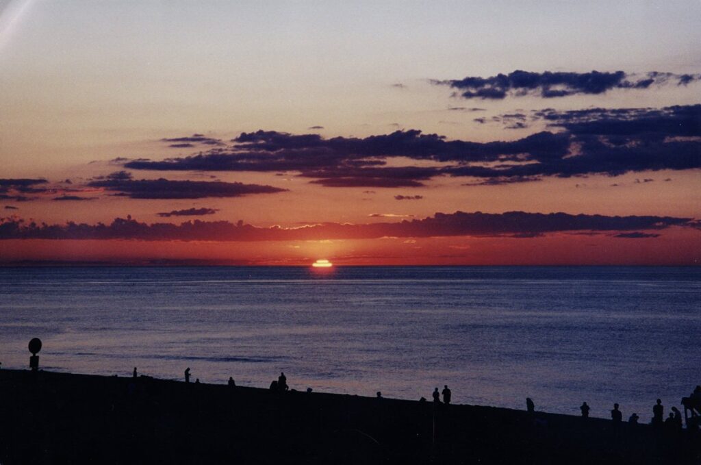 The sun setting into the ocean off Race Point Beach with people silhouetted on the sand
