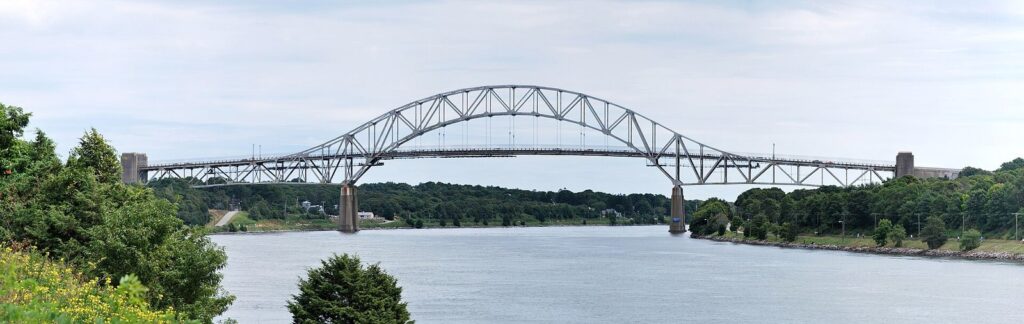 The steel arch of the Sagamore Bridge spanning the Cape Cod Canal between green banks