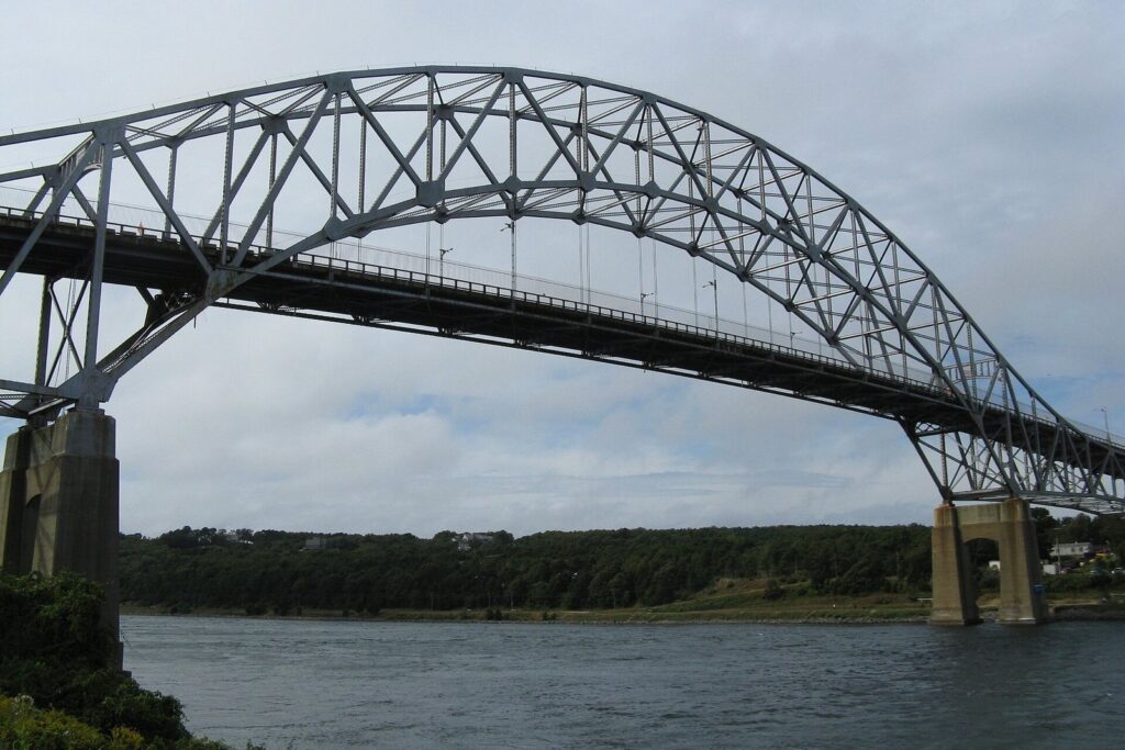 The steel arch of the Sagamore Bridge spanning the Cape Cod Canal, with wooded banks and an overcast sky