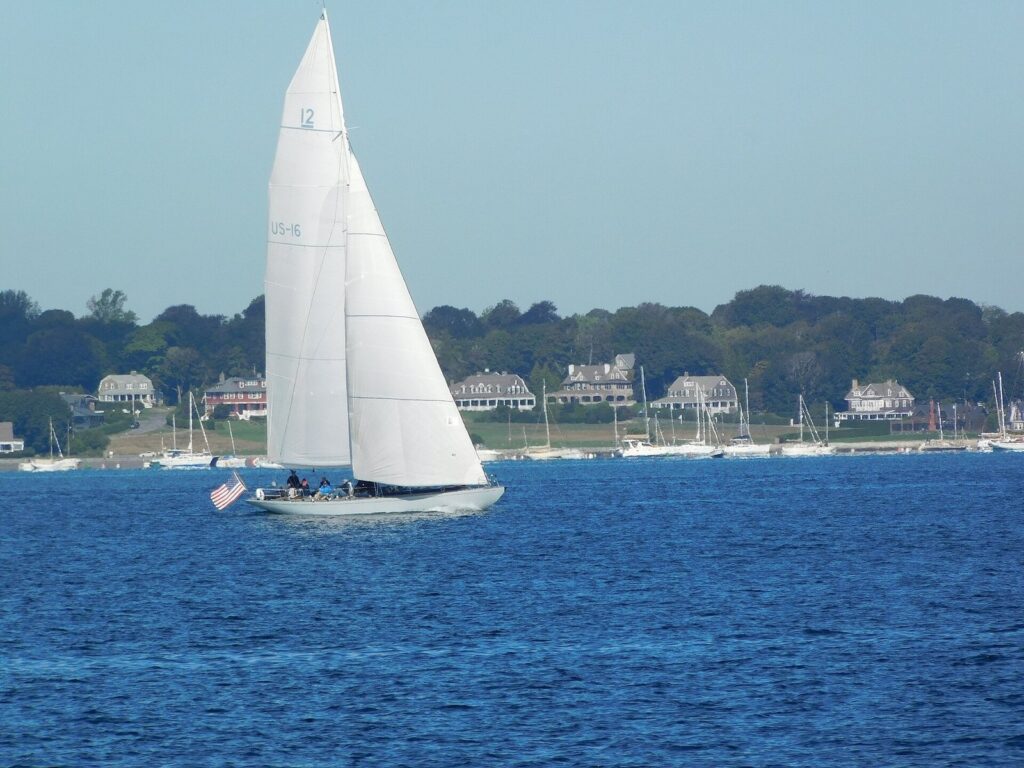 A classic white-hulled sailing yacht under full sail on blue water off the shore of Hyannis Port