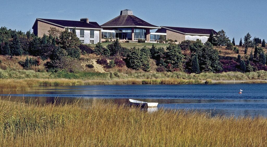 Salt Pond Visitor Center on a rise above Salt Pond in Eastham, with marsh grass and a small boat in the foreground