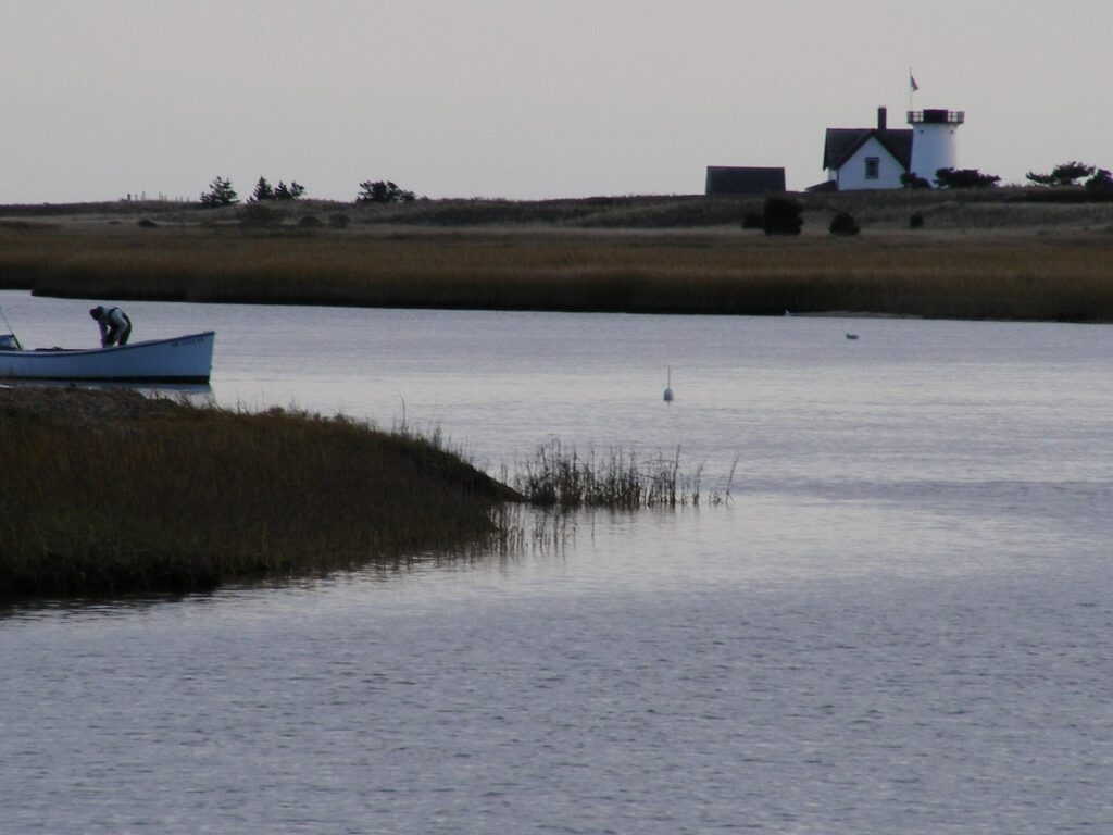 Stage Harbor Light and its keeper's house across a calm tidal inlet in Chatham, with a small boat in the foreground