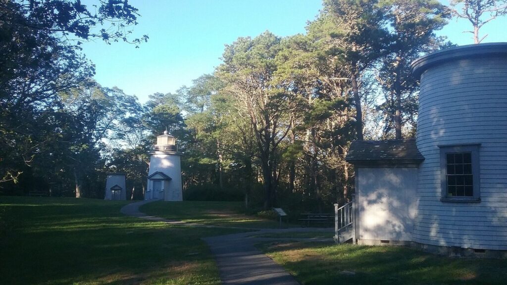 The small white Three Sisters Lighthouses standing in a grassy clearing among pine trees in Eastham