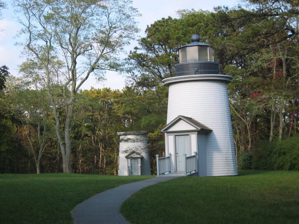 Two of the white wooden Three Sisters lighthouses standing in a grassy clearing in Eastham