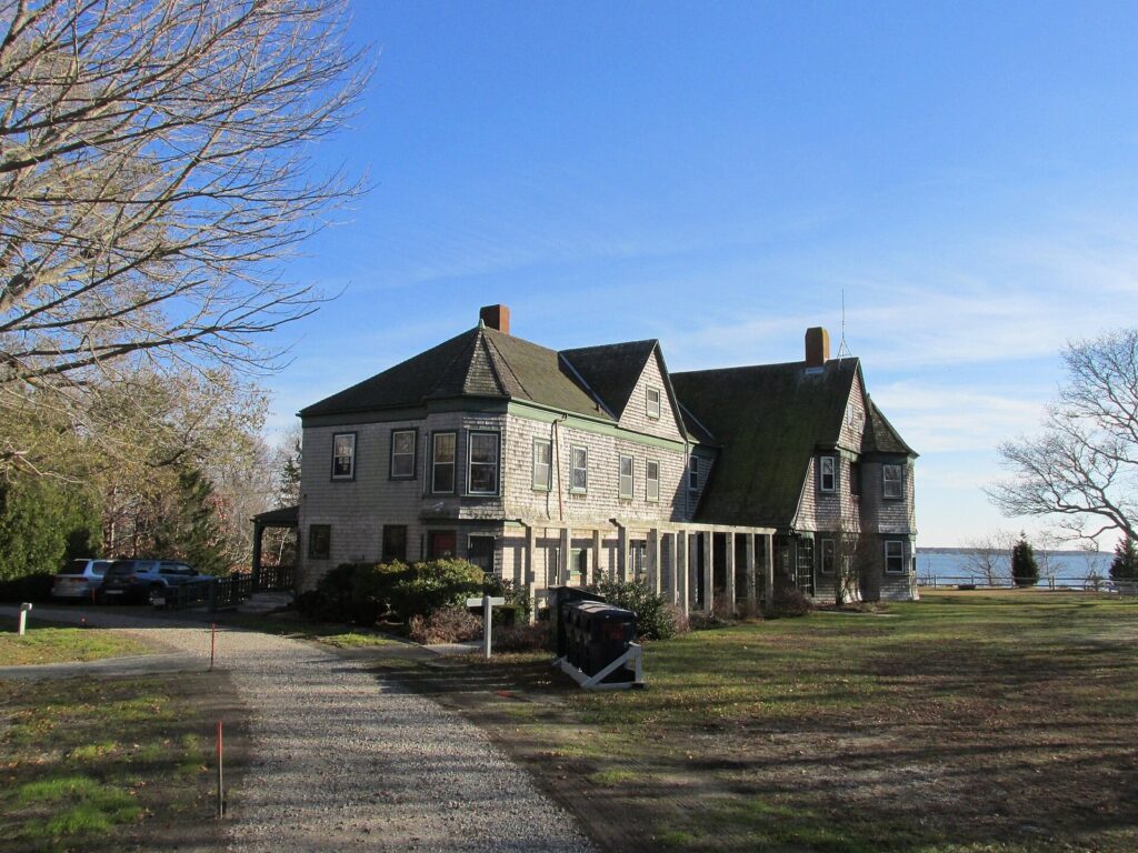 The shingled visitor center of the Waquoit Bay National Estuarine Research Reserve on a lawn above the bay