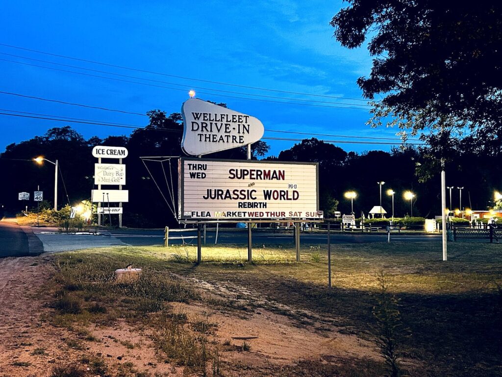 The Wellfleet Drive-In sign and marquee lit up at dusk beside Route 6
